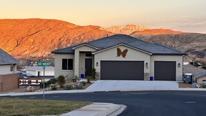 A modern two-story house with a butterfly mural on the front, garage doors, and a view of a mountainous landscape in the background. - Amazing VIEWS, NEW quiet home, bonus Fitness Room! (Hurricane)
