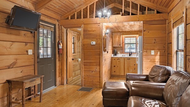 A log cabin interior with a wooden bench, leather sofa, and a television mounted on the wall.