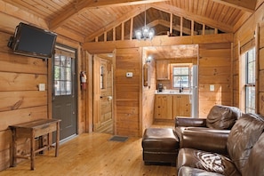 A log cabin interior with a wooden bench, leather sofa, and a television mounted on the wall.