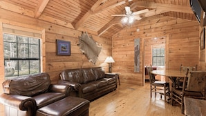 A log cabin interior with a leather sofa, wooden dining table, and chairs.