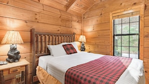 A wooden cabin bedroom with a bed, two bedside tables, lamps, and a window.