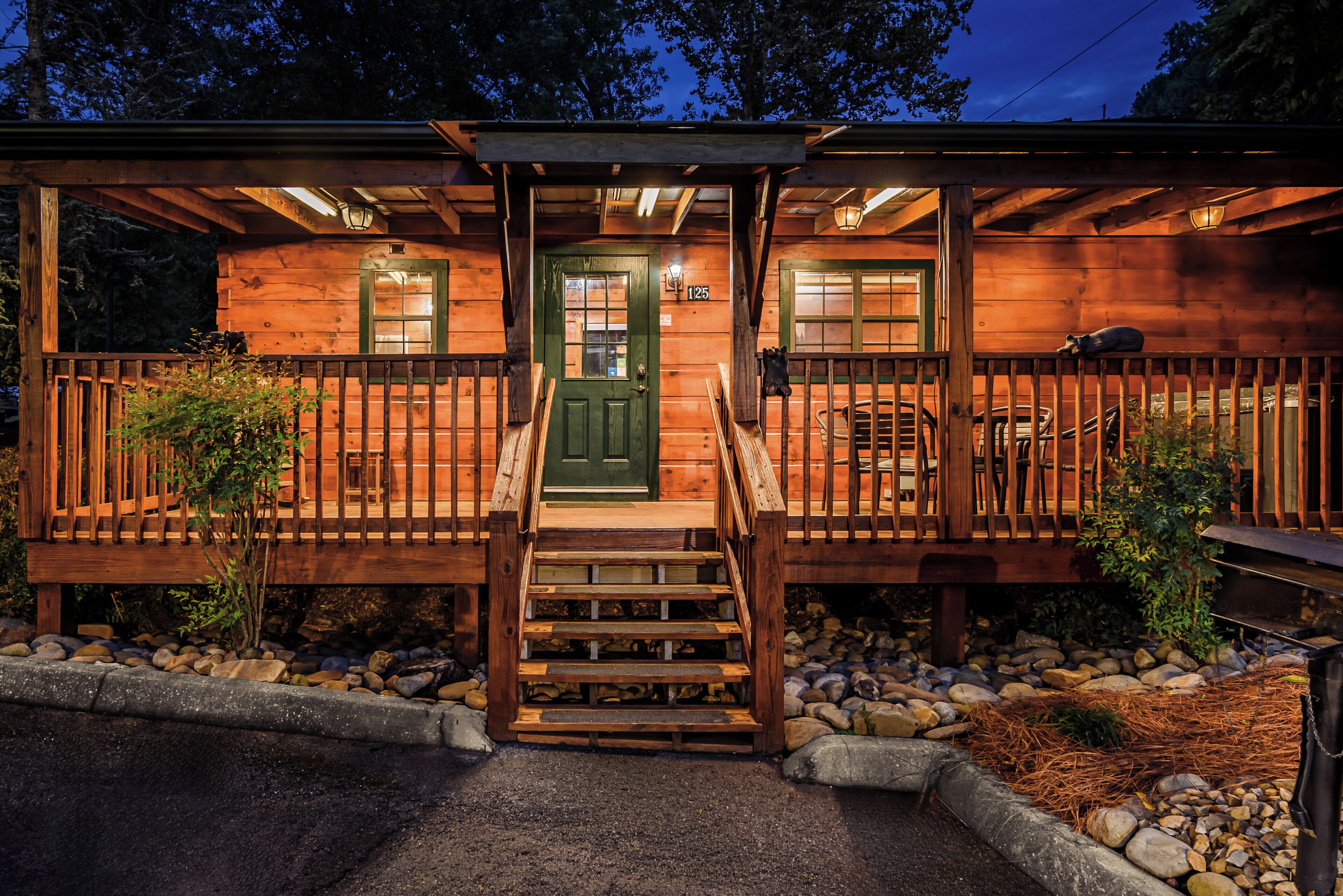A wooden cabin with a green door, a porch with a railing, and a staircase leading to the entrance.