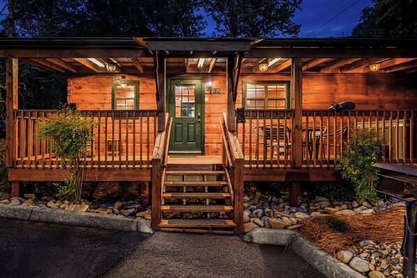 A wooden cabin with a green door, a porch with a railing, and a staircase leading to the entrance.