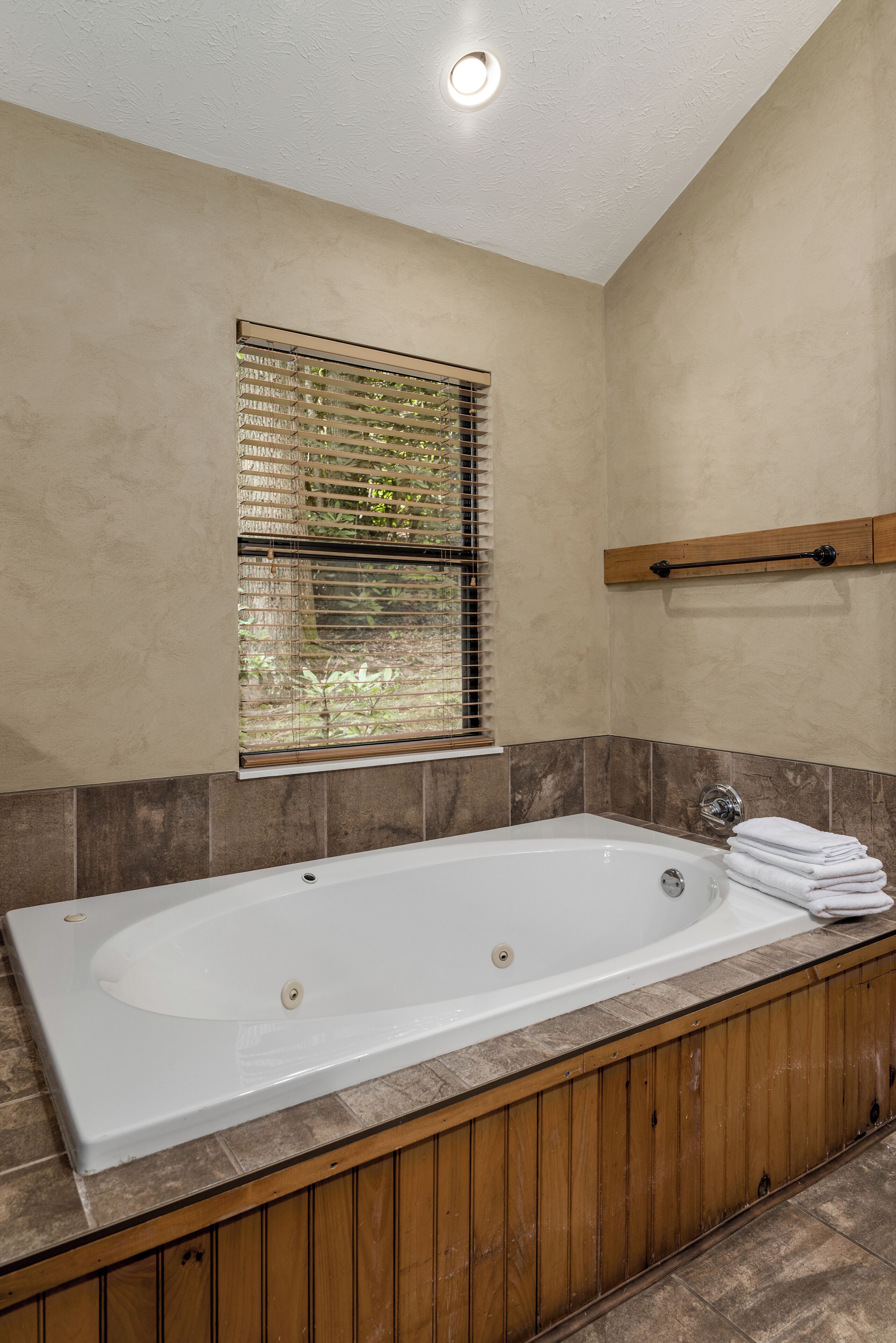 Ein modernes Badezimmer mit einer großen Badewanne, Holzvertäfelung, einem Fenster mit Jalousien und einem Handtuchhalter.