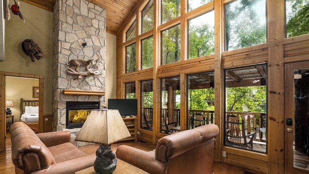 Un salón acogedor con chimenea de piedra, sofás de cuero y ventanas amplias con vistas al exterior.