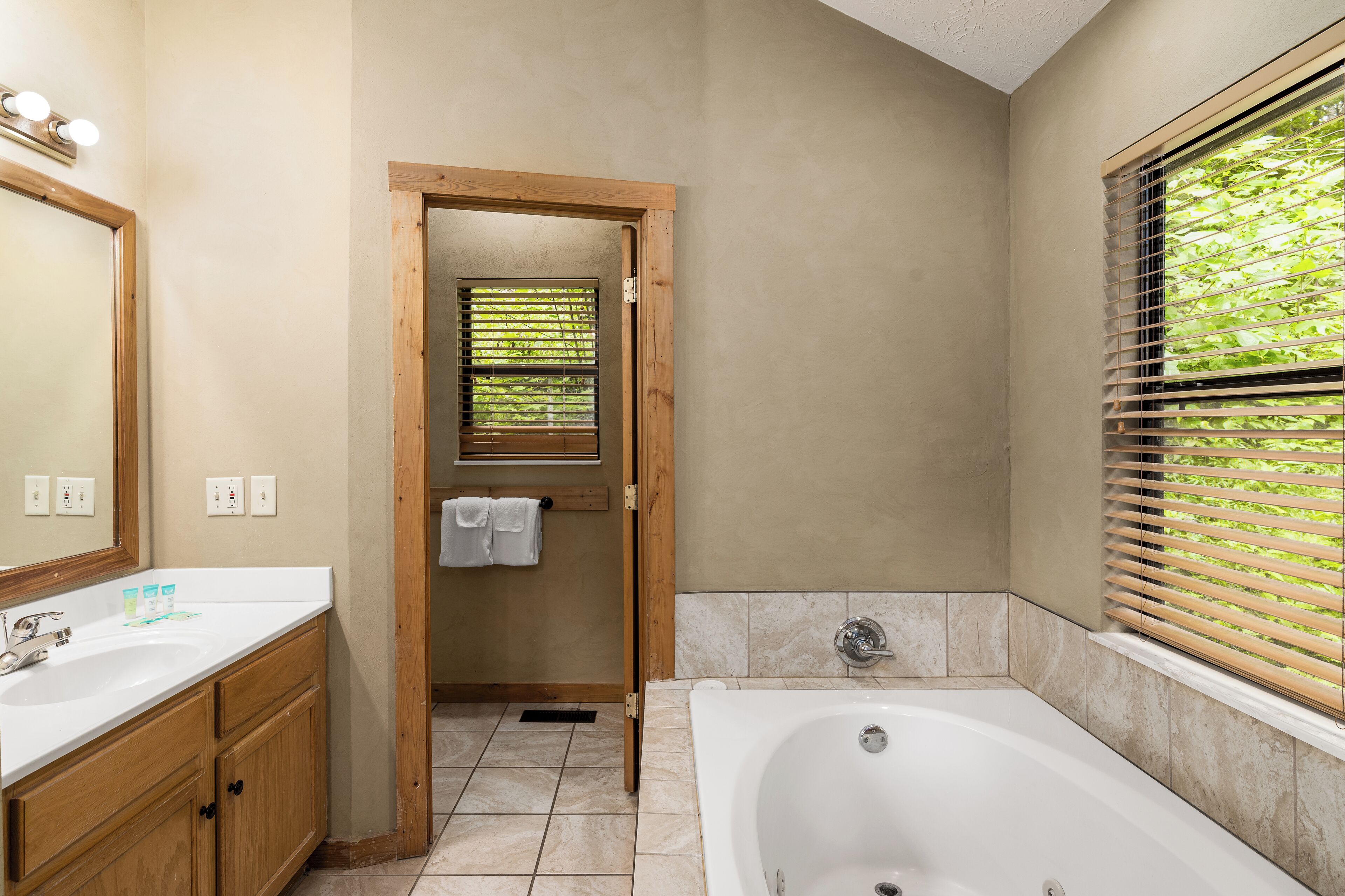 Un baño con bañera, armarios de madera, lavamanos y una ventana con persianas.