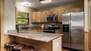 Una cocina con armarios de madera, un refrigerador de acero inoxidable, un microondas y una encimera de granito.