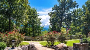 A stone pathway leading to a wooden fence, surrounded by lush greenery and flowering plants.