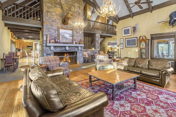 A spacious living room with leather sofas, a fireplace, and a stone wall.