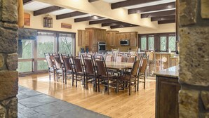 A spacious dining area with a large wooden table and chairs, surrounded by wooden cabinets and a stone wall.