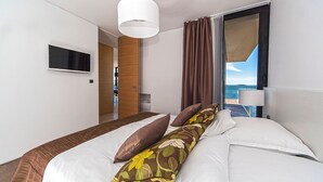 Een moderne hotelkamer met een groot bed, een aan de muur bevestigde televisie en uitzicht op zee door een groot raam.