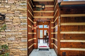 A log cabin interior with a stone wall on the left, a wooden door with the number 4020, and a view into a dining area.