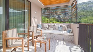Un balcon doté d’un plafond en bois, d’un espace salon avec des coussins et d’une vue sur des collines verdoyantes.