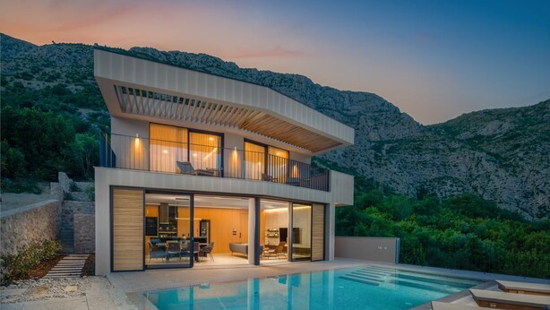 Une maison moderne à deux étages avec une piscine, entourée d’un paysage naturel.