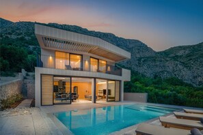 Une maison moderne à deux étages avec une piscine, entourée d’un paysage naturel.