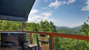 Eine Holzterrasse mit Whirlpool, Stühlen und einem Tisch mit Blick auf eine bewaldete Landschaft.