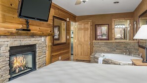 Ein Schlafzimmer mit Kamin aus Stein, einem an der Wand montierten Fernseher, einem Deckenventilator und einem großen Fenster.