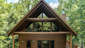 Una cabaña de madera con balcón, ventanas grandes y chimenea.