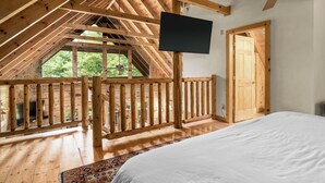 Un dormitorio con techo de madera, televisor montado en la pared, cama y vistas al exterior.