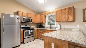 A kitchen with wooden cabinets, stainless steel appliances, a granite countertop, and a window with blinds. - Eagle’s Nest • Epic Smoky Mtn Views • Hot Tub (Sevierville)