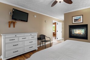 Un dormitorio con una cama grande, un aparador, un televisor montado en la pared, una chimenea y una puerta que da a un balcón.