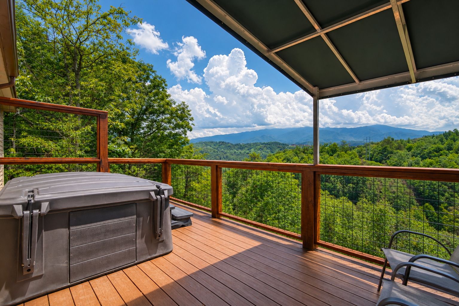 A wooden deck with a hot tub, overlooking a forested landscape with mountains in the distance.