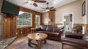 A living room with a brown leather sofa, a wooden coffee table, and a ceiling fan. - Eagle’s Nest • Epic Smoky Mtn Views • Hot Tub (Sevierville)