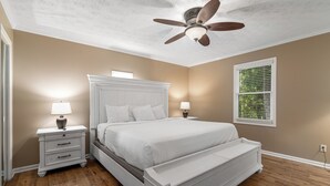 A bedroom with a white bed, wooden floor, ceiling fan, and two bedside tables with lamps. - Eagle’s Nest • Epic Smoky Mtn Views • Hot Tub (Sevierville)