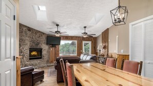 A spacious living room with a stone fireplace, leather sofas, a wooden dining table, and ceiling fans. - Eagle’s Nest • Epic Smoky Mtn Views • Hot Tub (Sevierville)