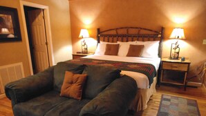 A room with a bed, a couch, two nightstands, and a door. - Dove's Nest: Beautiful, Pet Friendly Cabin Alongside a Creek near Downtown Gatlinburg (Gatlinburg)