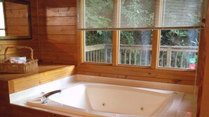 A wooden cabin with a large bathtub, wooden walls, and a window with a view of greenery. - Dove's Nest: Beautiful, Pet Friendly Cabin Alongside a Creek near Downtown Gatlinburg (Gatlinburg)