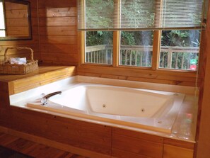 A wooden cabin with a large bathtub, wooden walls, and a window with a view of greenery.