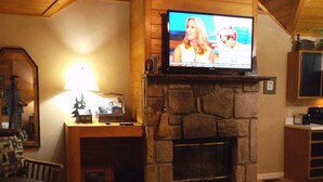 A cozy living room with a stone fireplace, a television mounted above it, a wooden coffee table, and a comfortable seating area. - Dove's Nest: Beautiful, Pet Friendly Cabin Alongside a Creek near Downtown Gatlinburg (Gatlinburg)