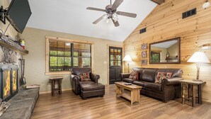 Un salon chaleureux avec une cheminée, des meubles en cuir, un plancher en bois et un ventilateur de plafond.