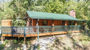 Une cabane en bois avec un toit vert, une véranda dotée d’une balustrade et une cheminée.