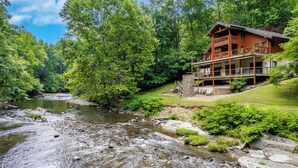 Une cabane en rondins dotée d’un balcon donnant sur une rivière, entourée d’une forêt dense.