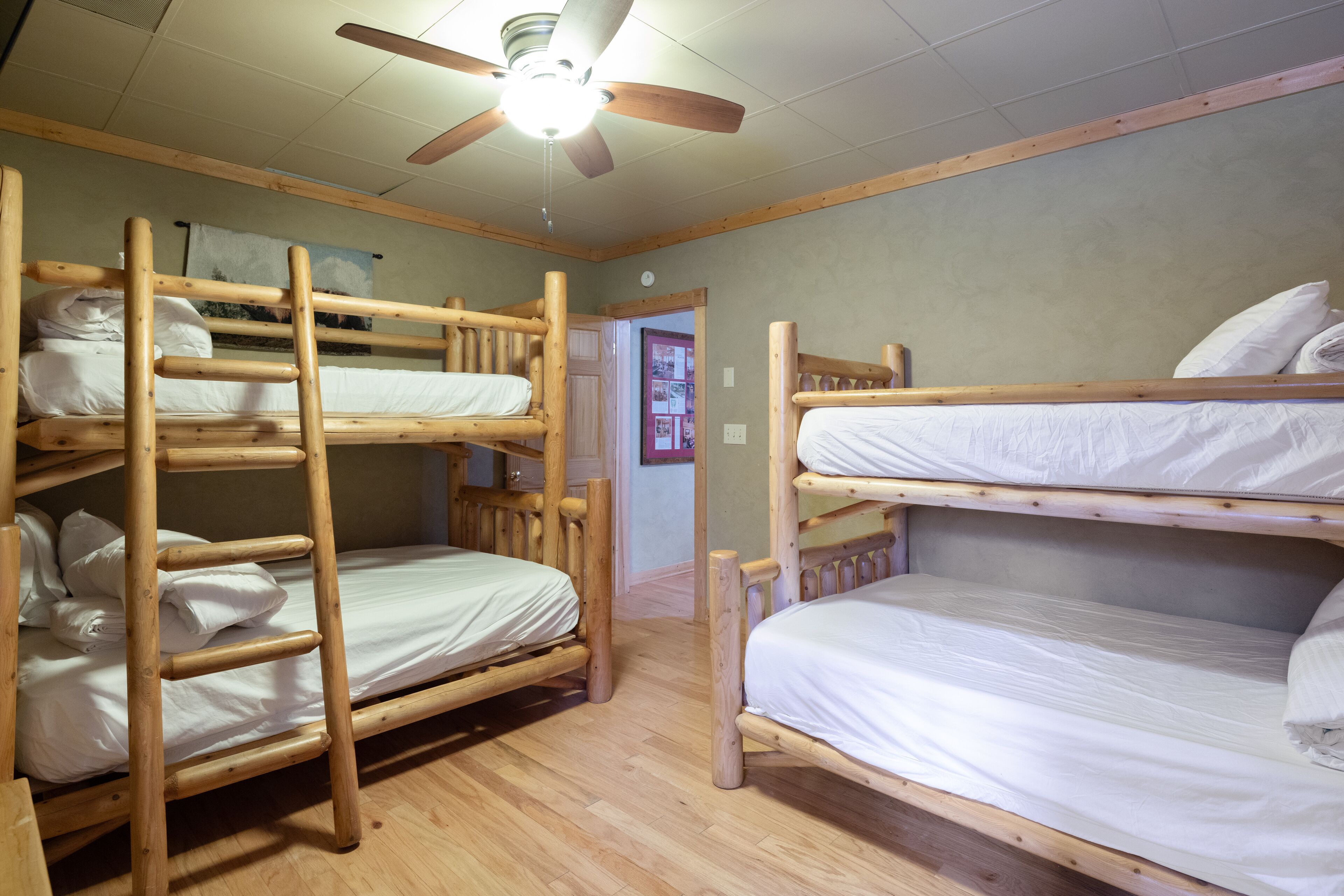 Une chambre avec un lit superposé en bois, un ventilateur de plafond et un luminaire.