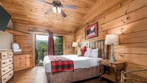 A wooden cabin bedroom with a bed, a nightstand, a chair, and a ceiling fan.
