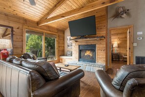 A log cabin interior with a fireplace, leather sofas, and a television mounted on the wall. - Mountain Memories: Mountain Cabin with Awe-Inspiring Views! (Sevierville/Pittman Center)