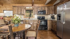A wooden cabin-style kitchen with a dining table, chairs, a refrigerator, a microwave, and a stove.