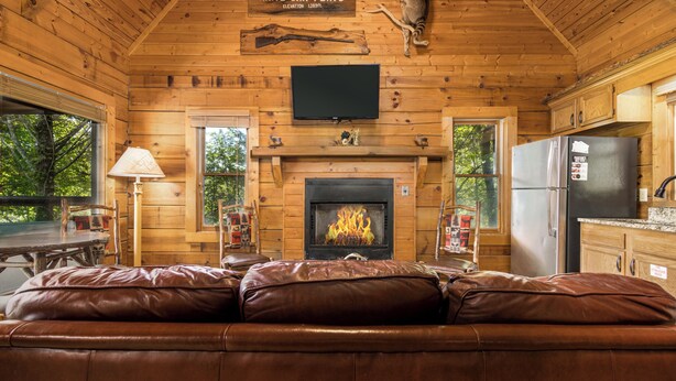 Ein rustikales Blockhaus-Interieur mit Kamin, Ledersofa, Holzwänden und einem an der Wand befestigten Fernseher.
