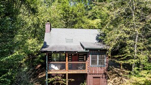 Eine zweistöckige Holzhütte mit Balkon, umgeben von dichtem Wald.