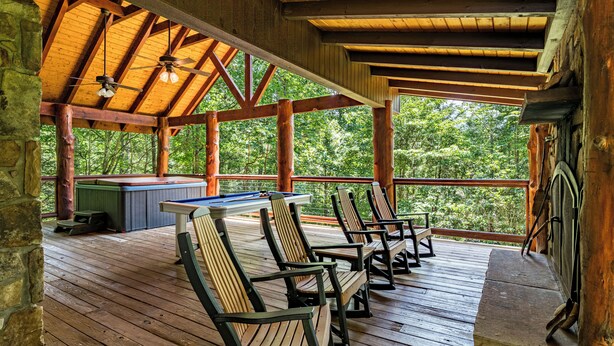 Eine überdachte Terrasse mit Holzstühlen, einem Billardtisch und einem Deckenventilator.