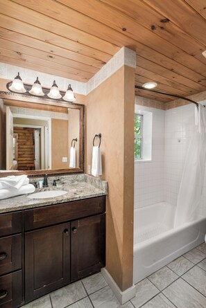 Ein Badezimmer mit Holzboden, einem großen Spiegel, einem Waschbecken mit dunklen Holzschränken, einer Badewanne und einem Fenster.