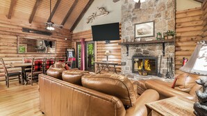 Ein rustikales Holzhaus-Interieur mit Kamin aus Stein, einer Ledersofa, einem Holzesstisch und einem flachbildfernseher an der Wand.