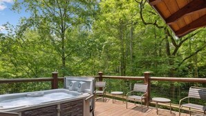 Une terrasse en bois avec un jacuzzi, des marches en pierre et des chaises en métal.