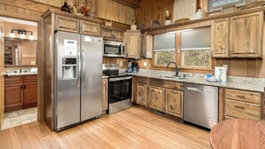 Une cuisine dotée de meubles en bois, d’appareils électroménagers en acier inoxydable, d’un plan de travail en granit et d’une fenêtre avec des stores.