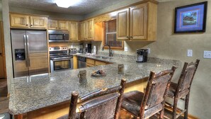 Una cocina con encimeras de granito, armarios de madera, electrodomésticos de acero inoxidable y una isla grande con taburetes de bar.