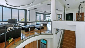 Een ruime woonkamer met een hoge plafond, grote ramen en uitzicht op de omgeving.