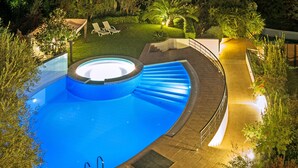 A swimming pool with a hot tub, surrounded by a deck with steps leading into the water.